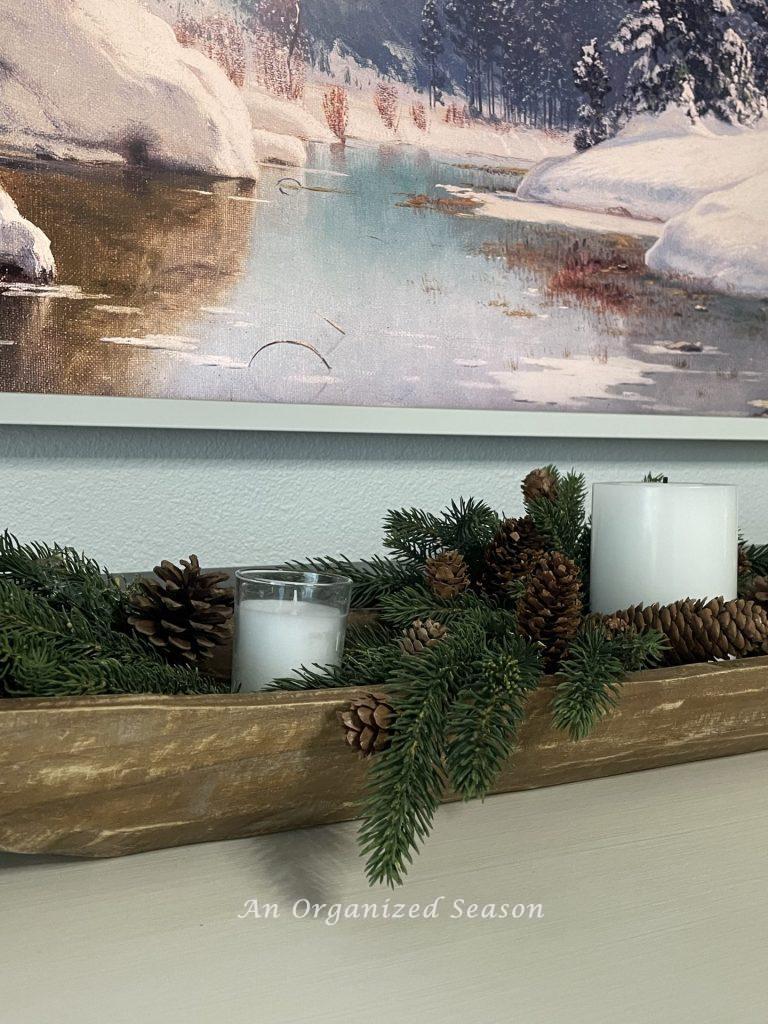 A dough bowl filled with evergreen, pinecones, and white candles. 