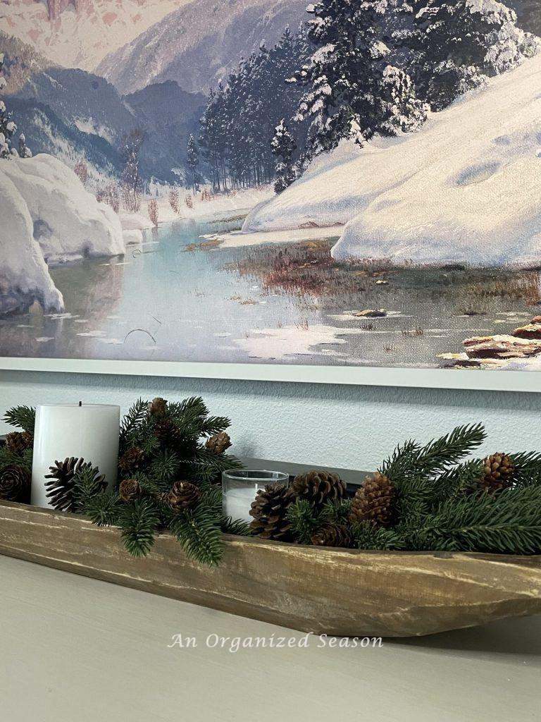 A dough bowl with evergreen branches, pinecones, and white candles. 