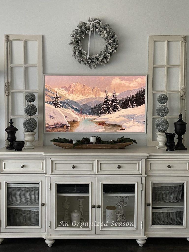 A TV console table decorated for Winter with a picture tv showing a painting of snow covered mountains.