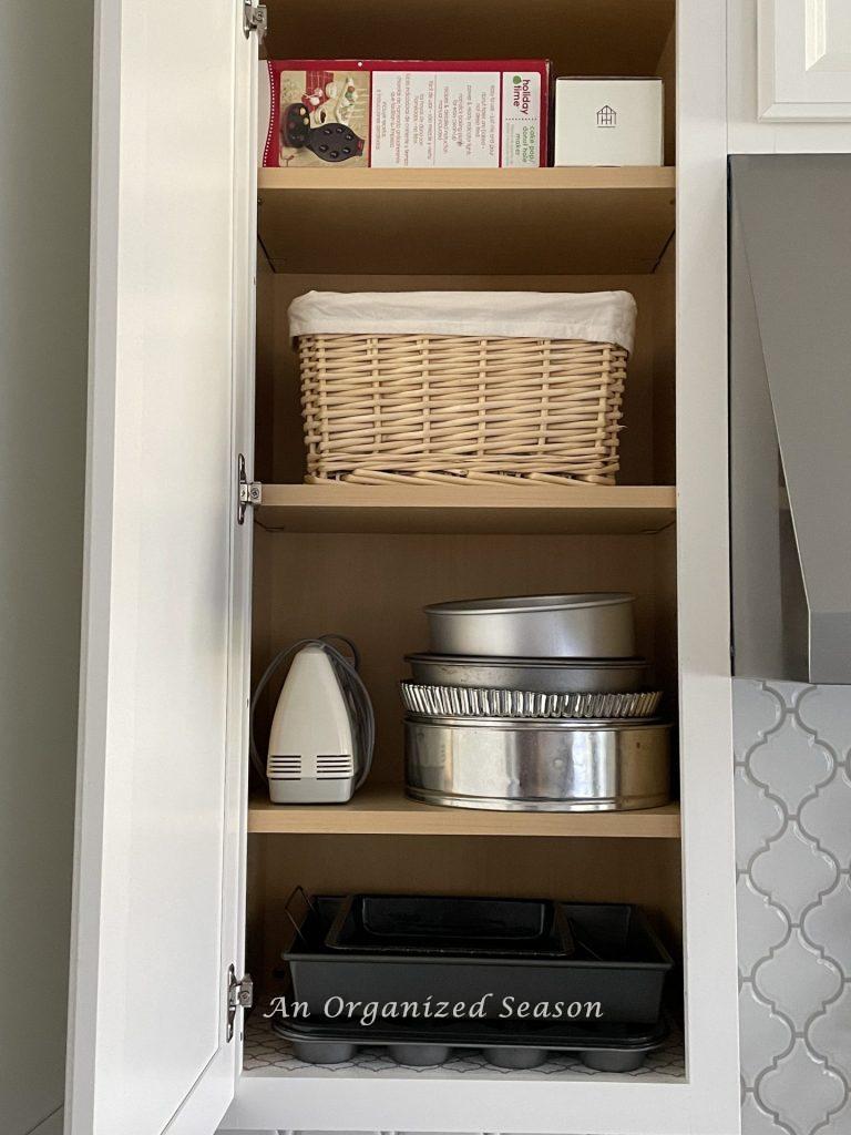 An organized kitchen cabinet with baking tools and a basket storing small items. 