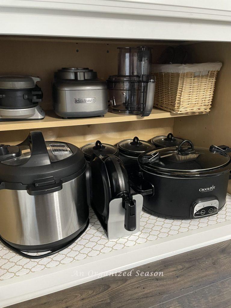 An organized kitchen cabinet containing small appliances.