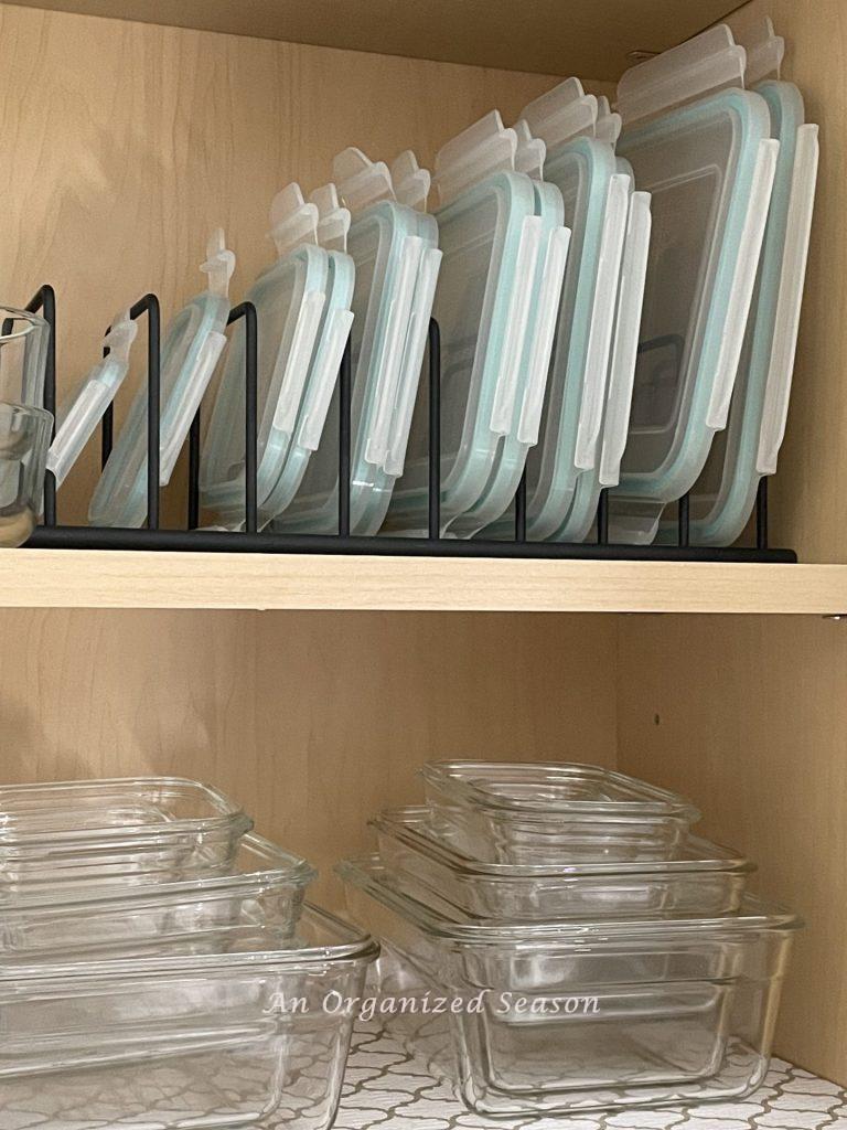 Organized glass food storage containers that are stacked and the lids are separated by a wire organizer. 
