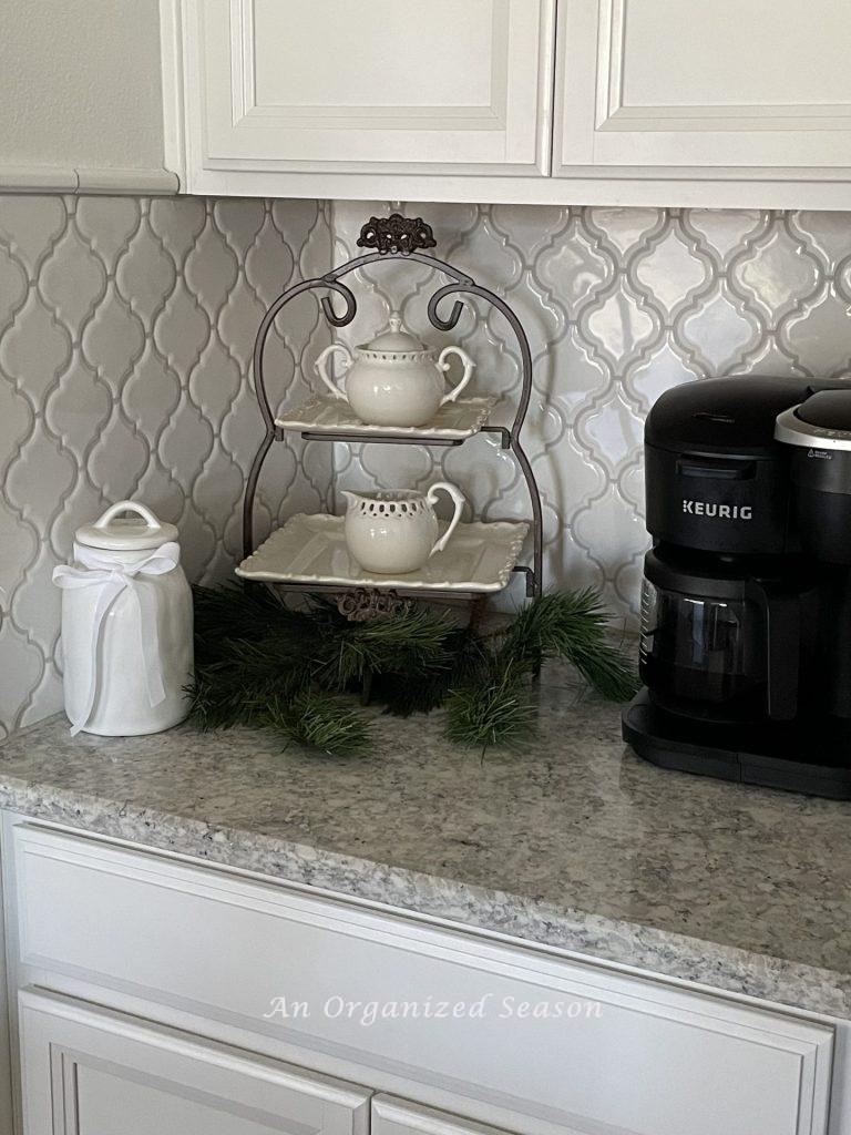 A tiered tray holds cream and sugar bowls with a coffee pot and white canister on either side. 