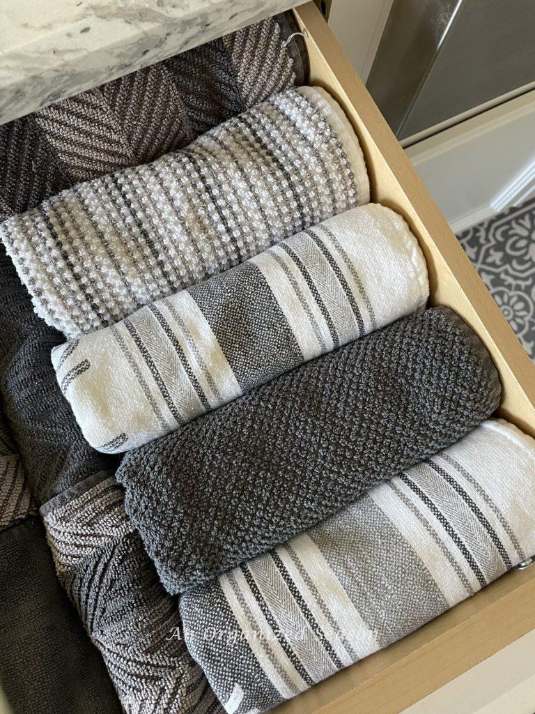 Gray and white dish towels rolled in a kitchen drawer. 