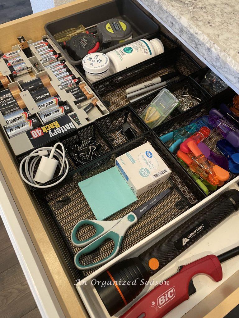 An organized kitchen junk drawer using different size dividers and a battery organizer.
