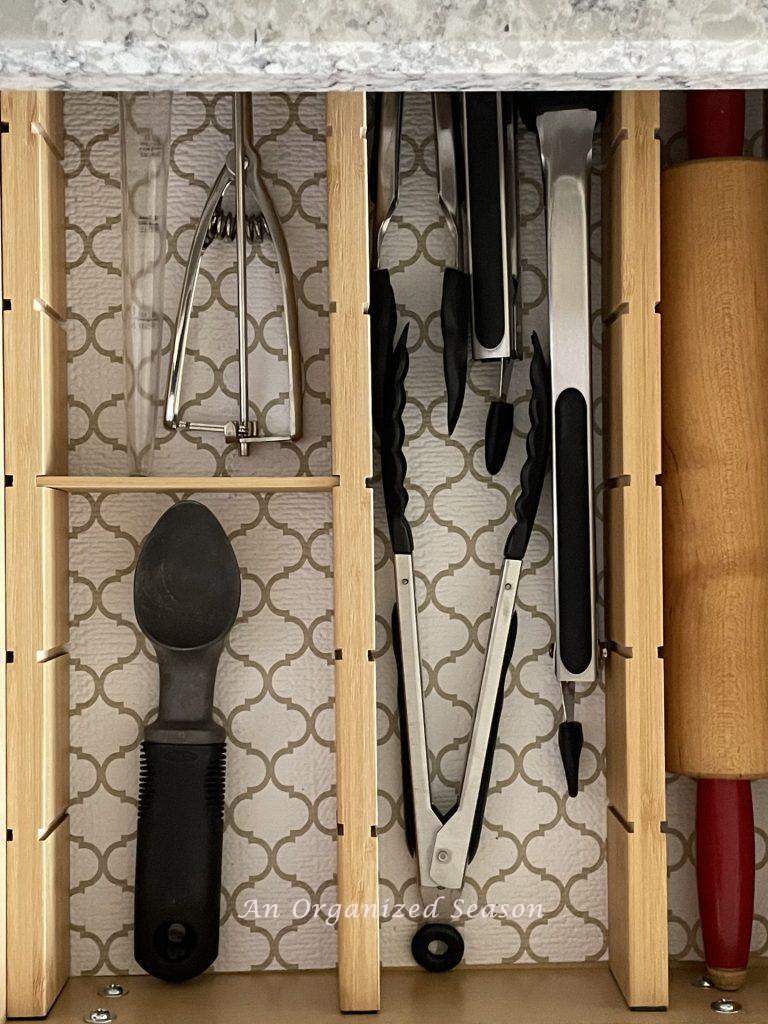 Bamboo dividers in a kitchen drawer help organize a rolling pin, tongs, an ice cream scoop, and baster.