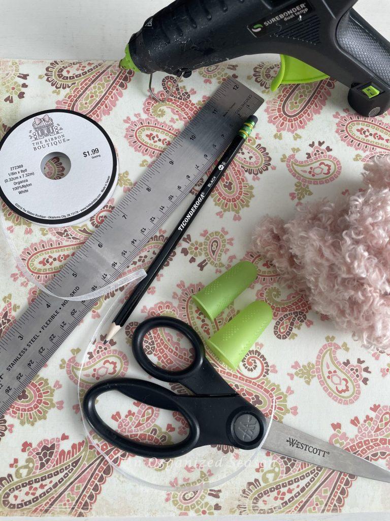 Scrapbook paper, hot glue gun, finger protectors, ruler, scissors, pencil, ribbon, and yarn. Items to make cute Valentine's hearts.