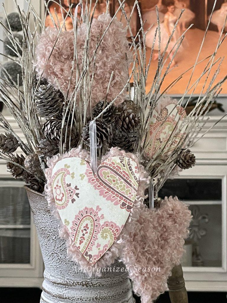 Valentine's hearts hanging from white branches covered in pinecones. 