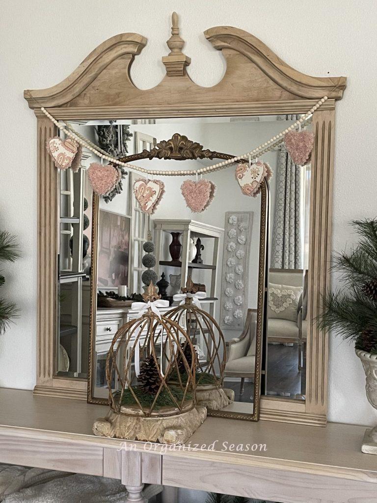 A mirror draped with a wood bead and Valentine's heart garland.