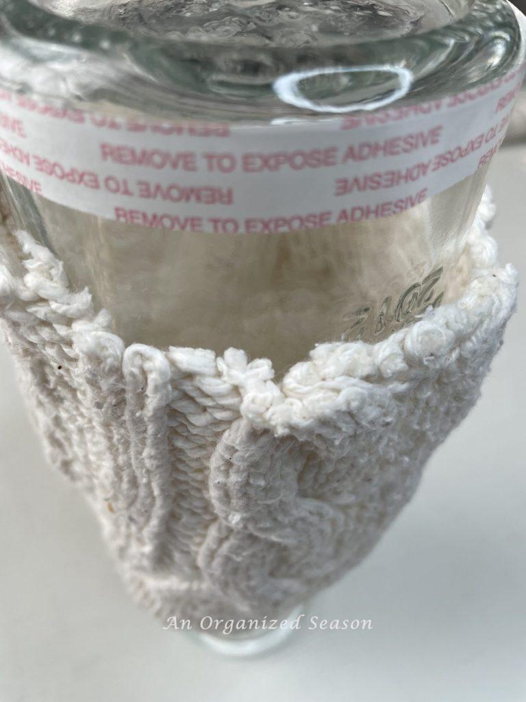 Double sided tape stuck to the bottom of a glass vase, step three for how to make cozy home decor with sweaters.