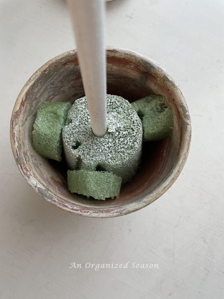 A dowel rod stuck into styrofoam covering the bottom of a flower pot.