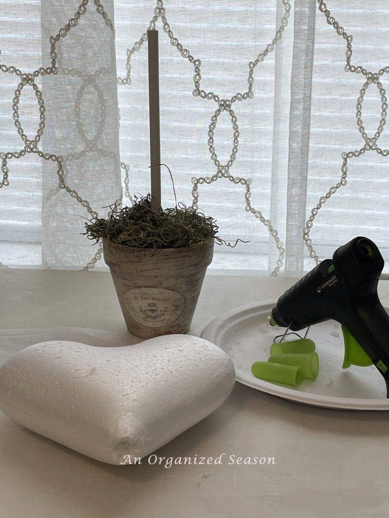 A styrofoam heart, glue gun, finger protectors, and a flower pot.