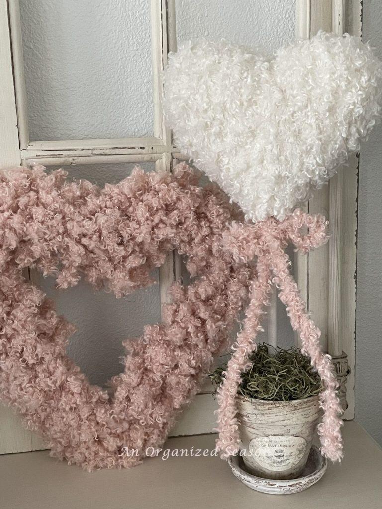 A white yarn topiary with pink bow next to a pink fluffy heart.