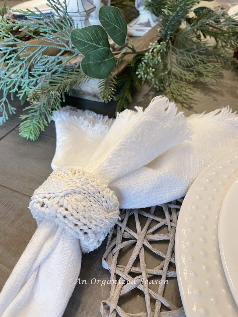 A napkin ring made from a cable knit sweater holds a white cloth napkin. 