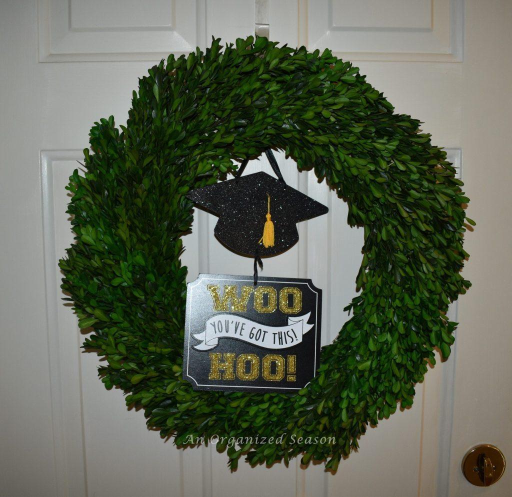 Boxwood wreath with a graduation sign hanging on it.