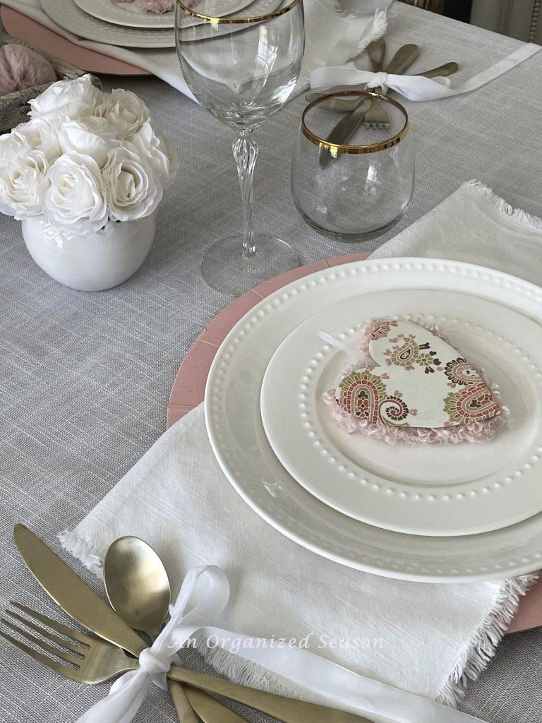 A place setting and white roses on a dining room table. 