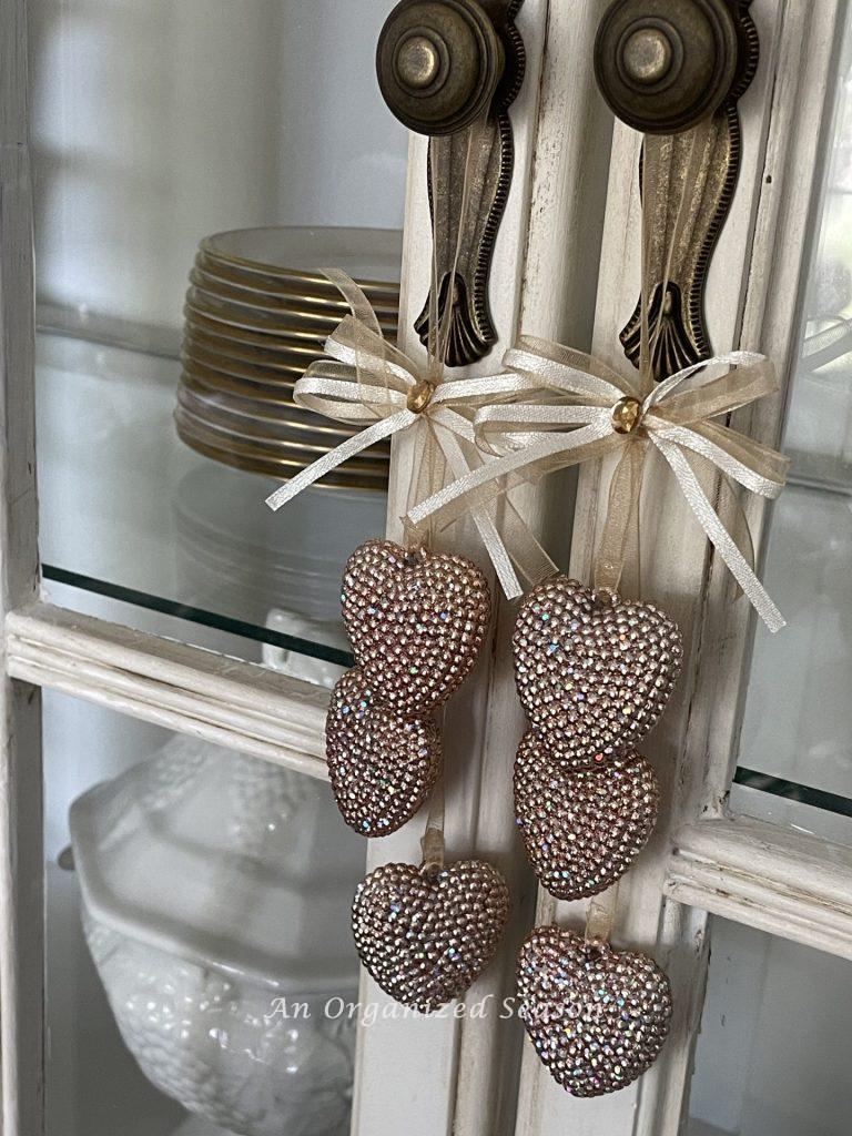 Heart ornaments hang from a knob on a china cabinet. 