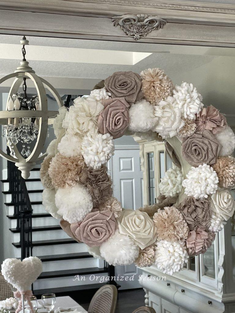 A pom-pom and rosette wreath hanging on a mirror. 