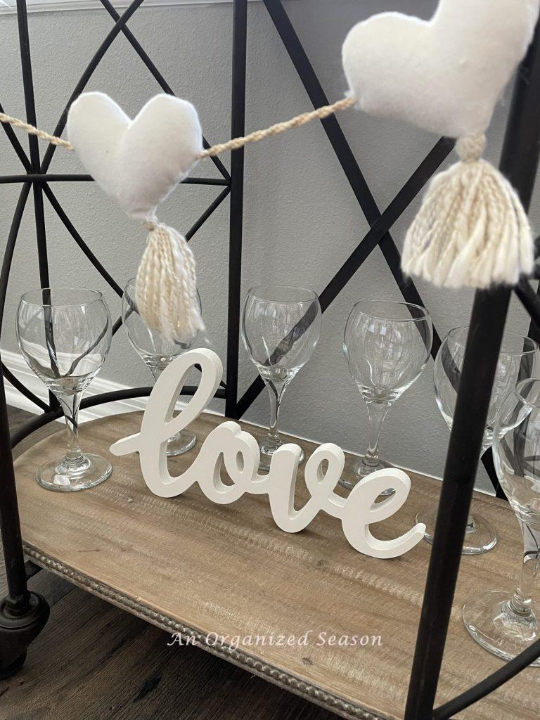 Heart garland, wine glasses, and a "love" sign on a bar cart, 