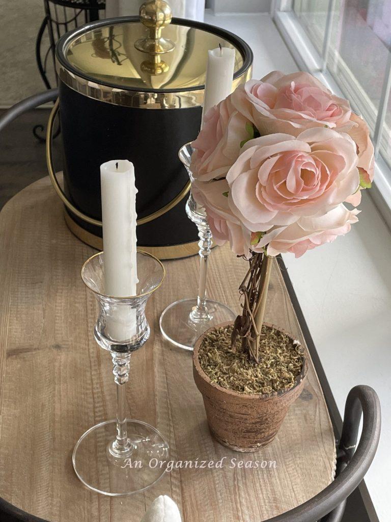 Ice bucket, white candles in crystal candleholders, and a pink rose topiary,