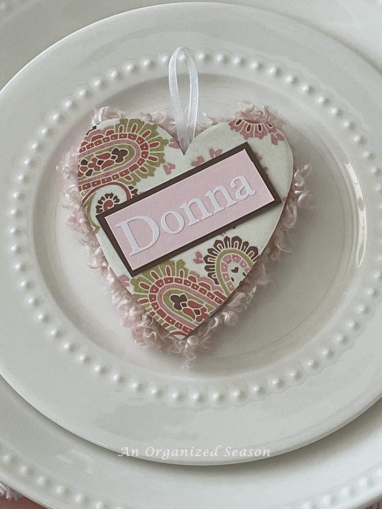 A heart with the name "Donna" sitting on a white plate and set on a table decorated for Galentine's day. 