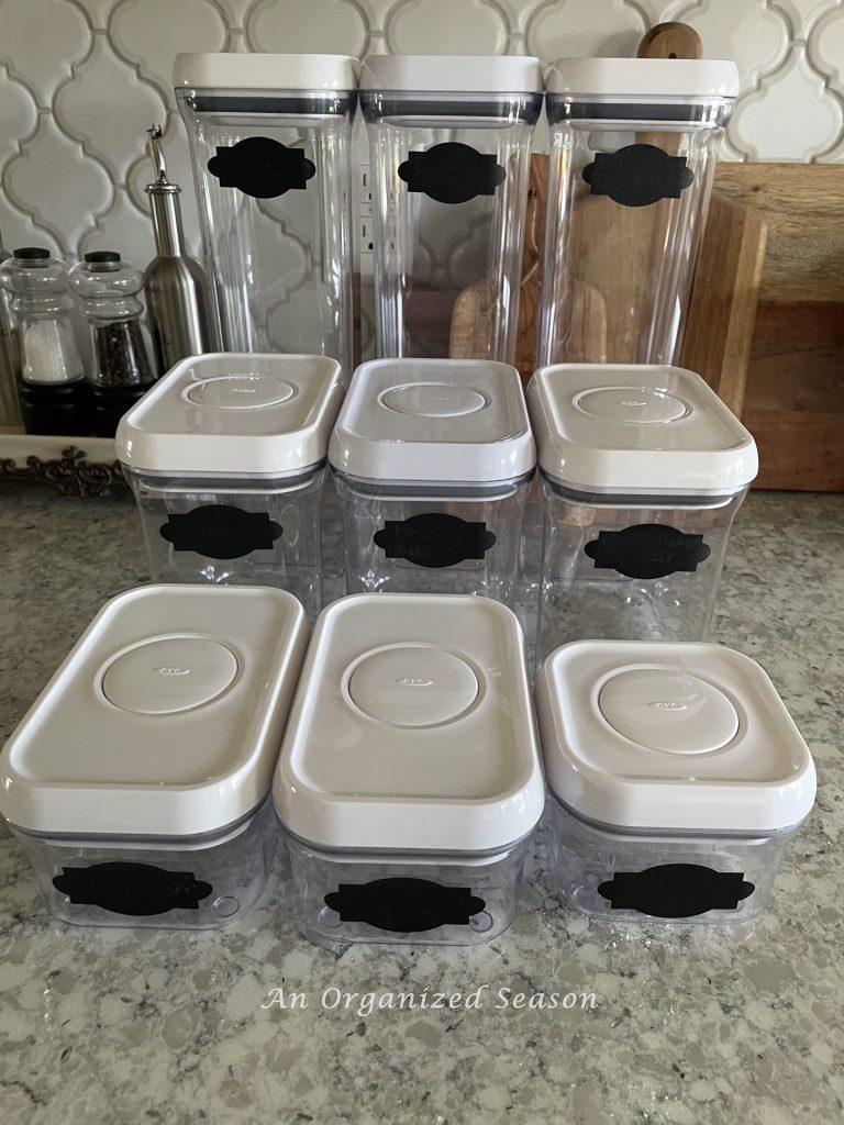 Nine empty Oxo canisters sitting on a kitchen counter. 