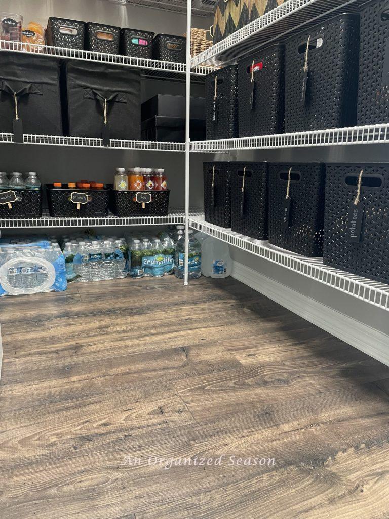 A pantry organized with black plastic bins and fabric cubes. 