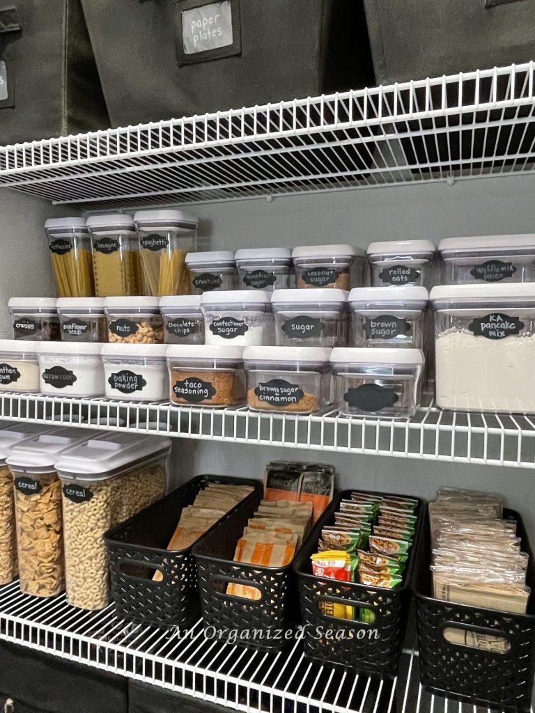 A pantry organized with Oxo containers and black plastic bins. 