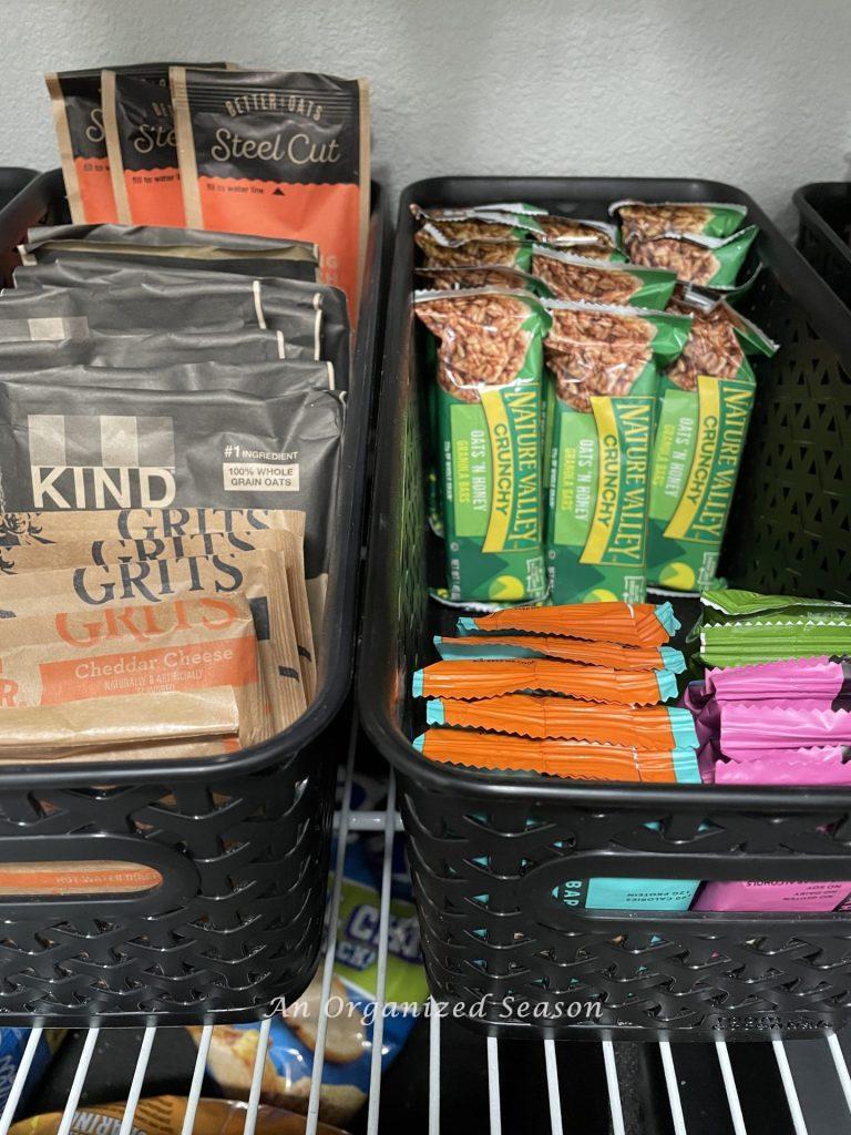 Oatmeal, granola bars, and protein bars stored in black containers in a pantry. 