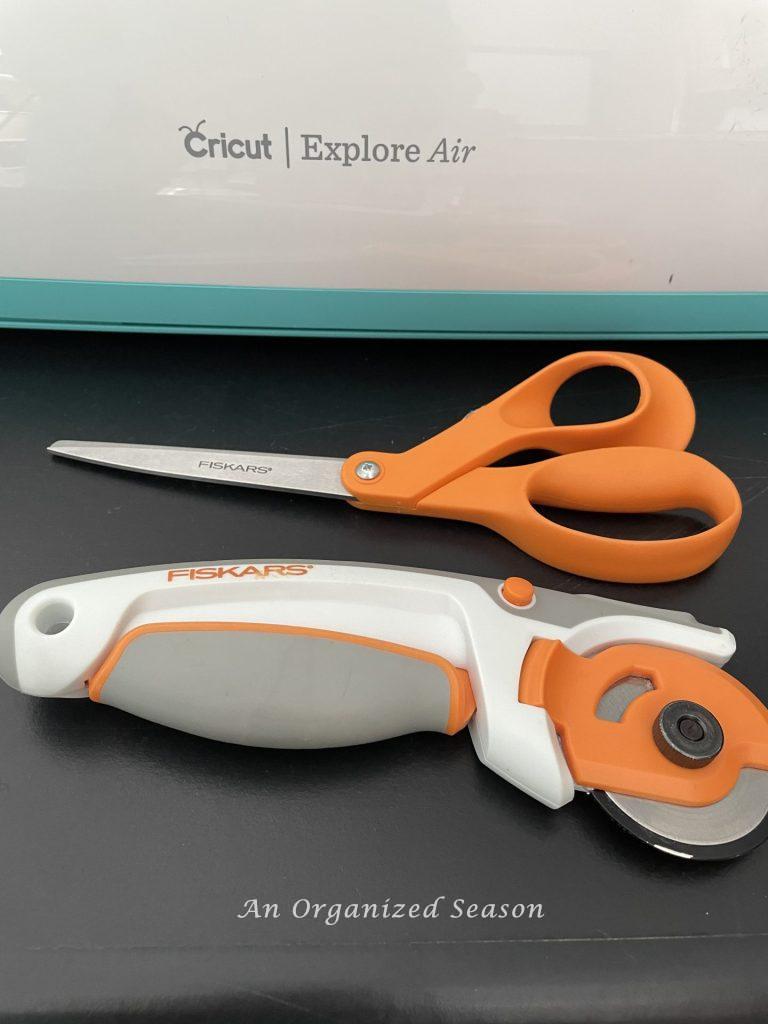 Cricut cutting machine with rotary and scissors in front of it. 