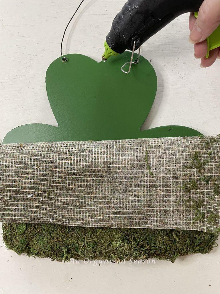 Step three in a DIY St. Patrick's makeover is to hot glue the moss to the sign. 