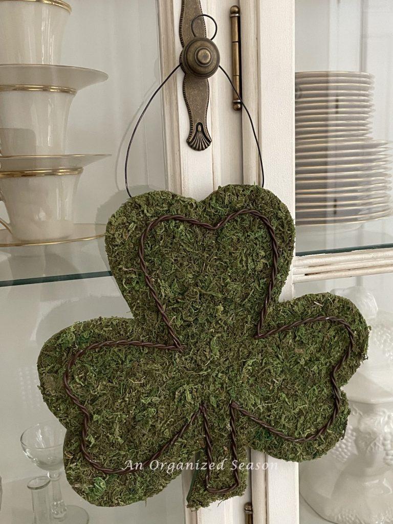 A moss shamrock hanging on a china cabinet door. 