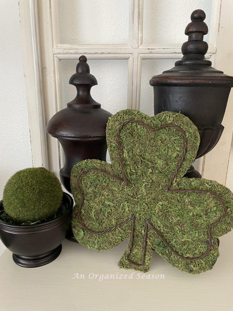 A moss shamrock leaning against two brown finial statues. 