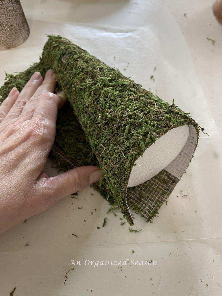 A styrofoam cone being wrapped in moss to make moss mushroom home decor.