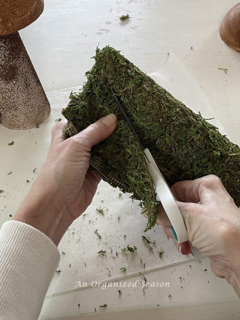 Someone cutting excess moss from a cone to make moss mushroom home decor.