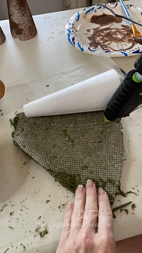 Someone hot gluing moss to a cone.
