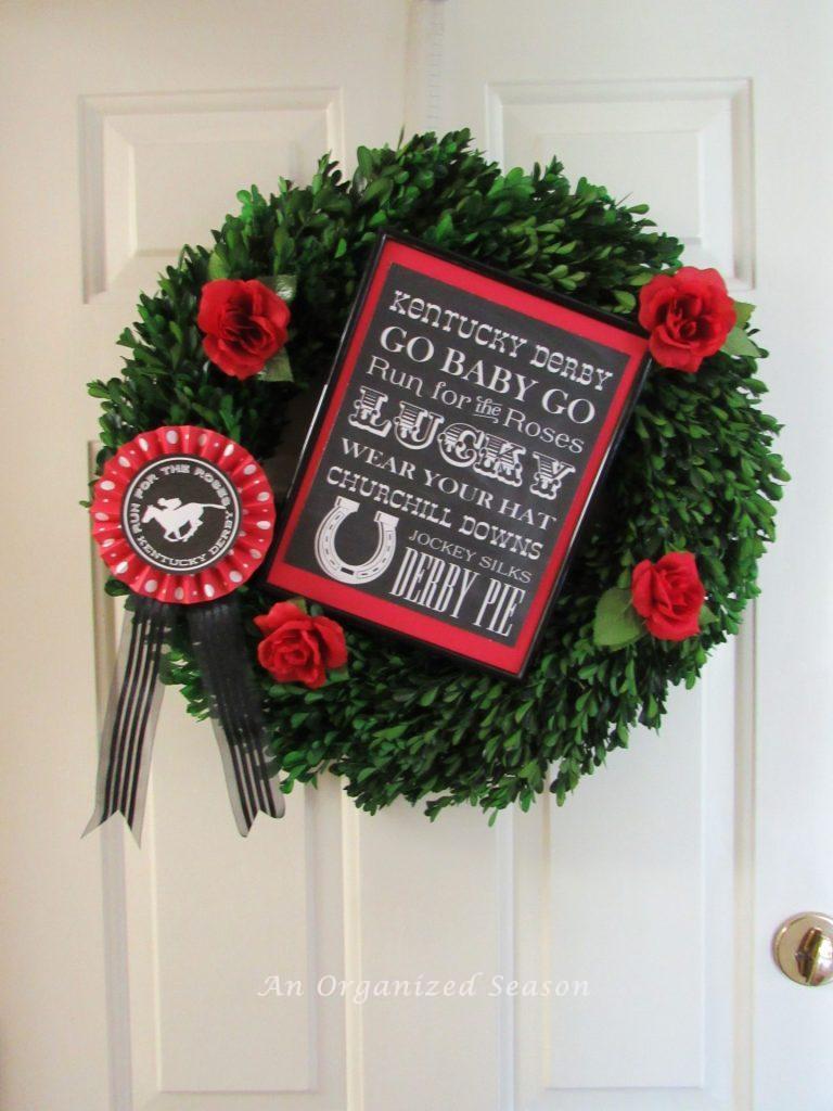 Boxwood wreath with red roses, a ribbon, and a Kentucky Derby photo.