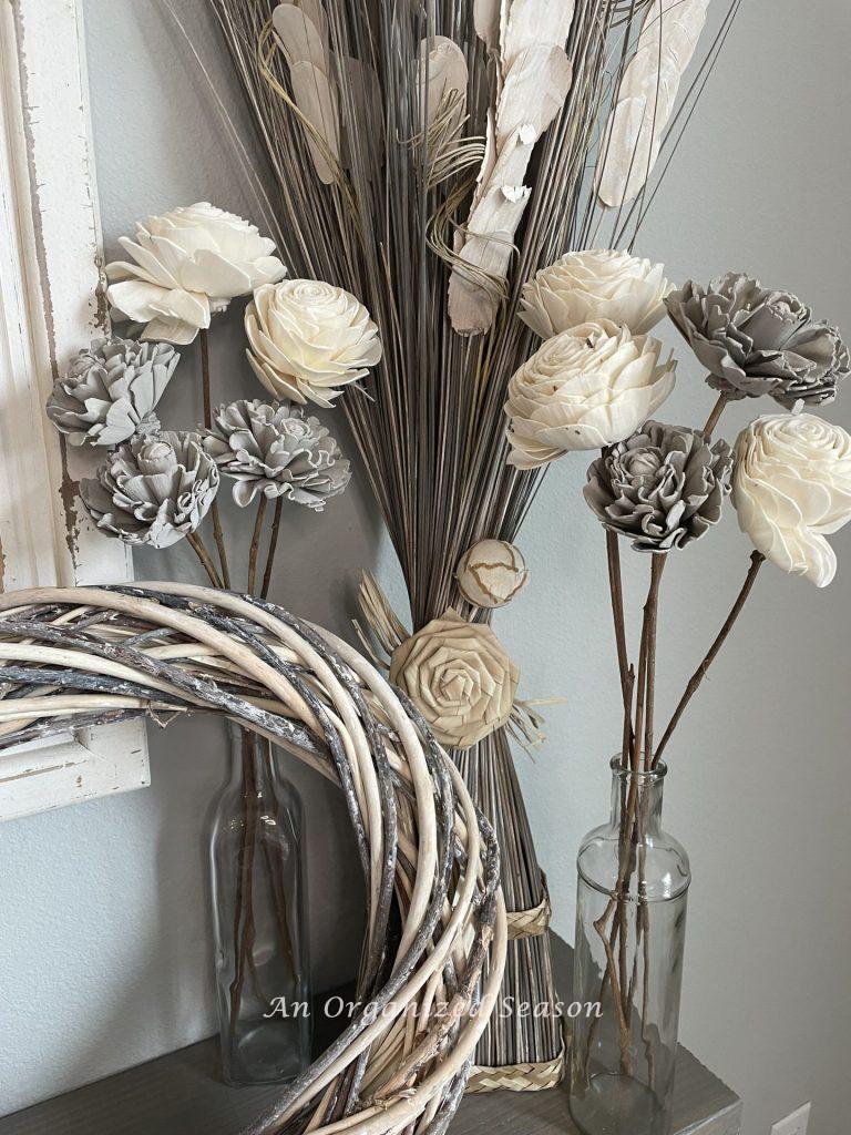 Gray and white wood flowers in glass vases with a wreath. 