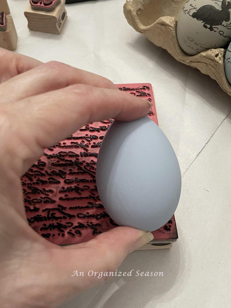 Roll an egg across a stamp is step three to  learn how to paint and stamp unique Easter eggs