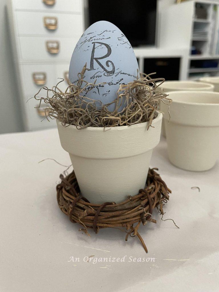 An egg with the initial "R" sitting on a mini flower pot. 