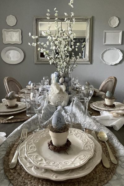 Easter table decorated with flowering branches in vase filled with eggs.