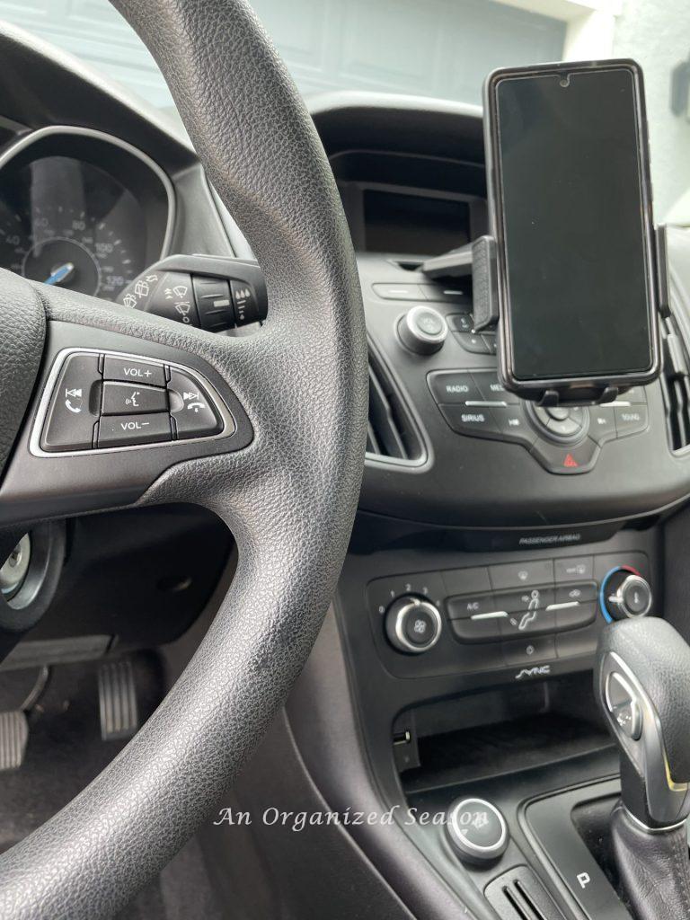 A car dashboard with a phone holder in the CD slot. 