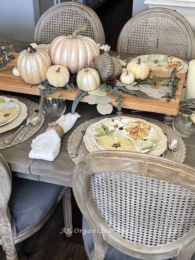 A table decorated for Thanksgiving with a wood tray holding pumpkins. 