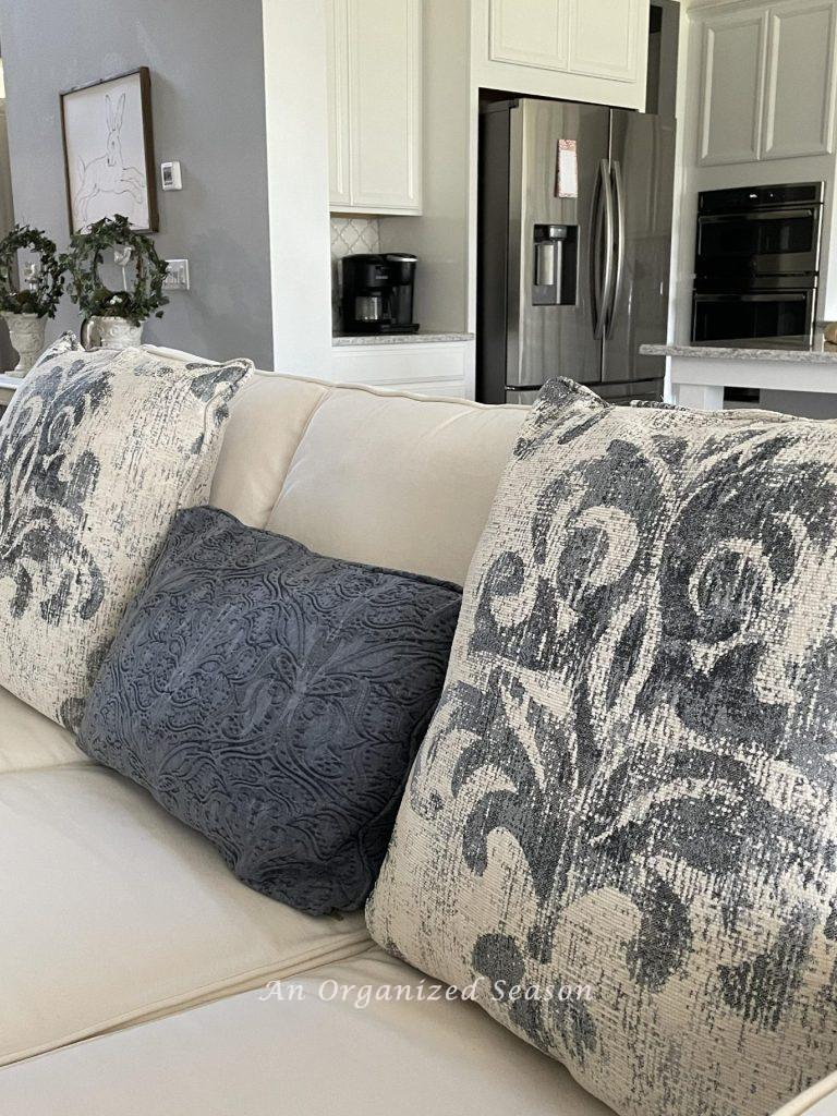 Two large blue and white pillows and a blue denim pillow on a white couch. 