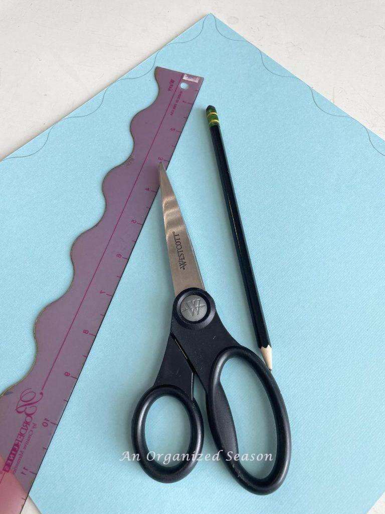 Blue cardstock, a scalloped ruler, scissors, and a pencil.