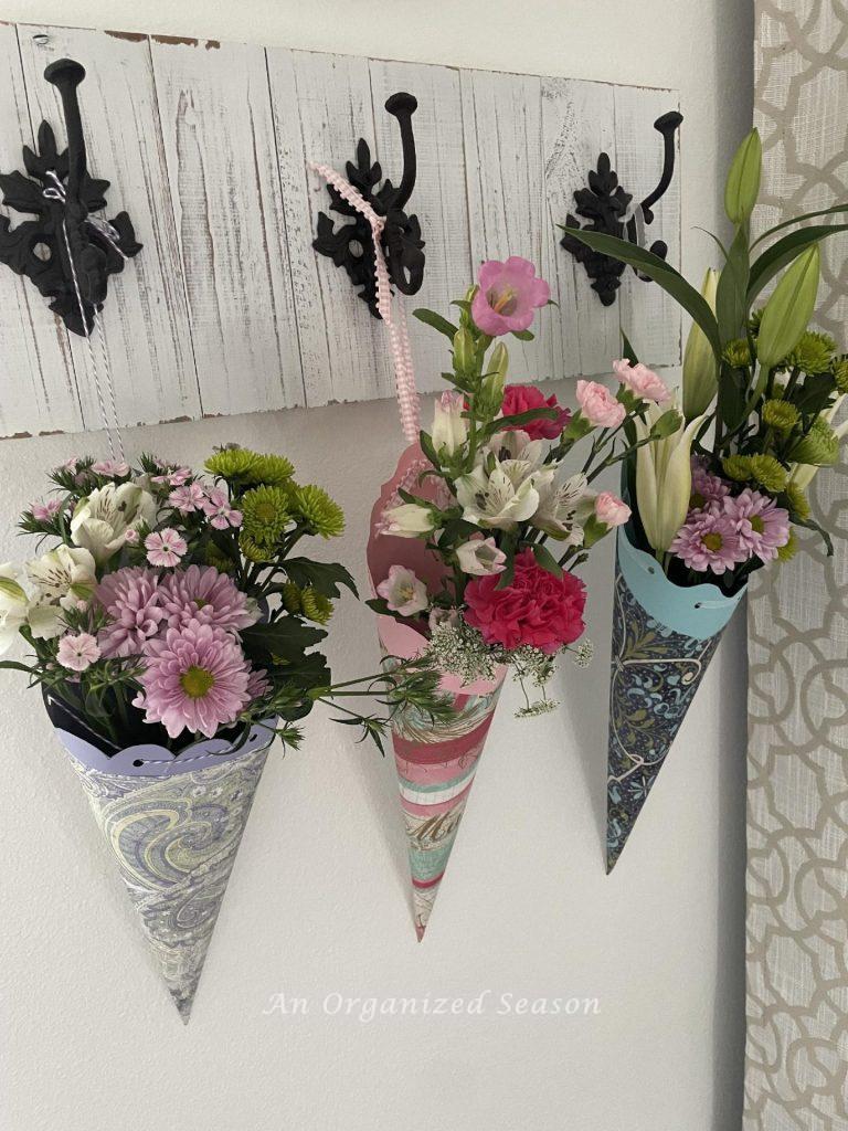 Three paper baskets filled with flowers hanging on a coat rack. 