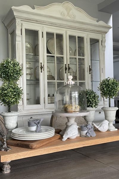 Wood tray with feet and handles on a dining room table, holding topiaries, a cake stand, and birds.