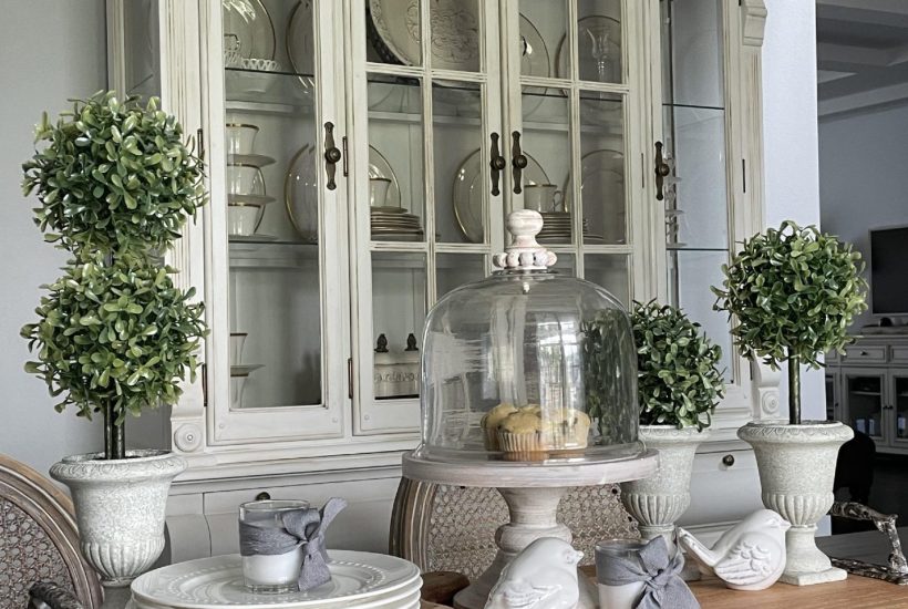 Wood tray with feet and handles on a dining room table, holding topiaries, a cake stand, and birds.