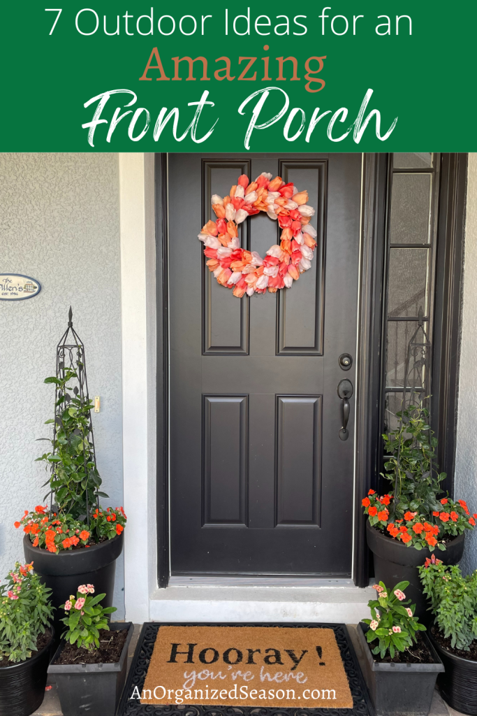 Black front door with tulip wreath and flower containers with orange flowers on each side of door. 