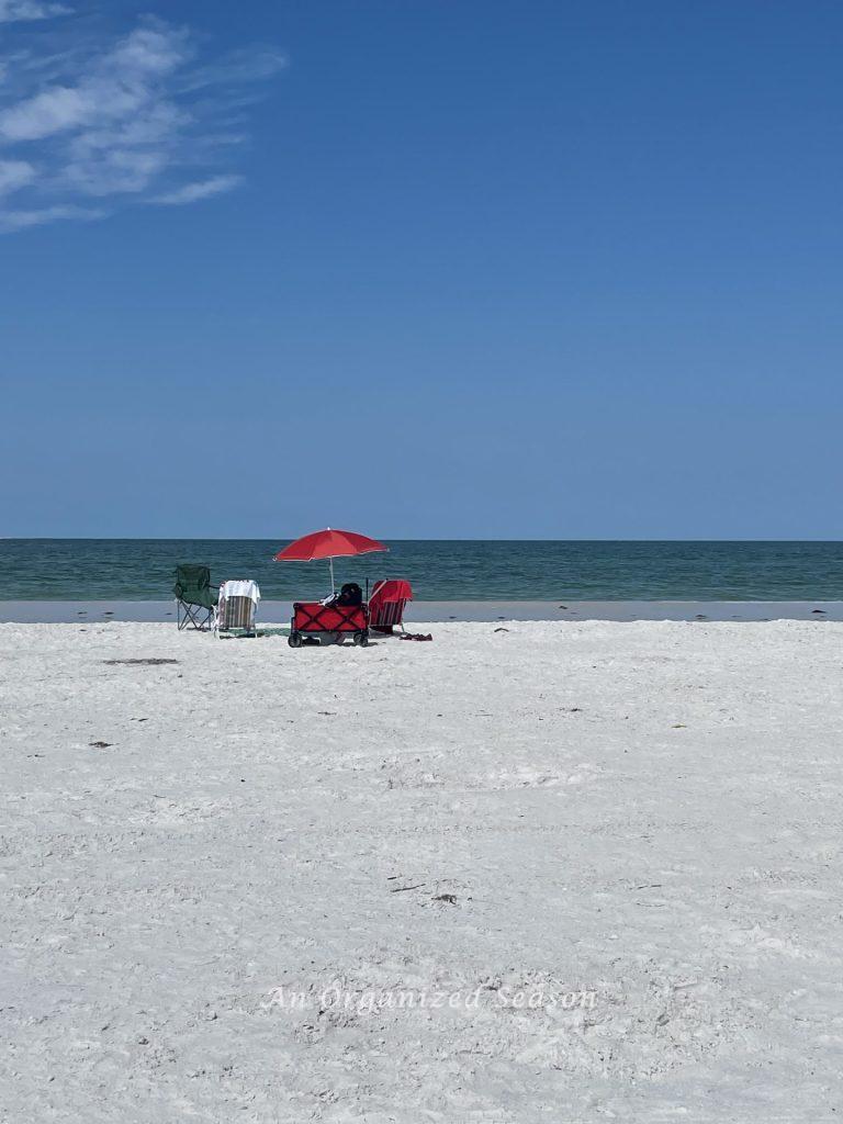 Wagon, beach chairs, and umbrella set up on a beach.